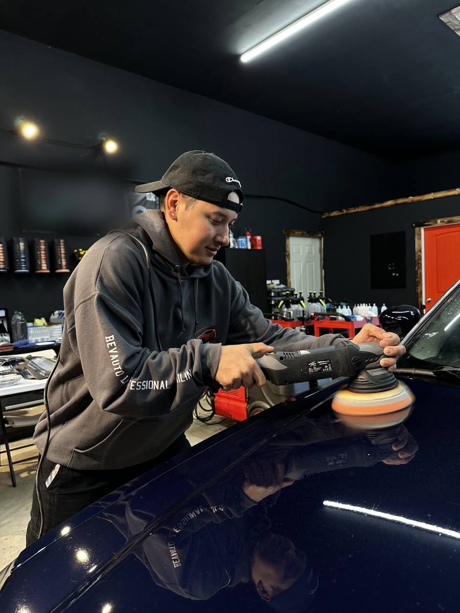 Quintin Harris, owner of Revauto Lux, machine polishing a dark blue vehicle in the shop